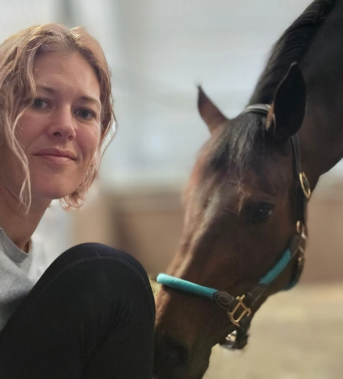 A quiet, affectionate moment between Sophia and Saffy, a brown Thoroughbred mare in the wooden stables.